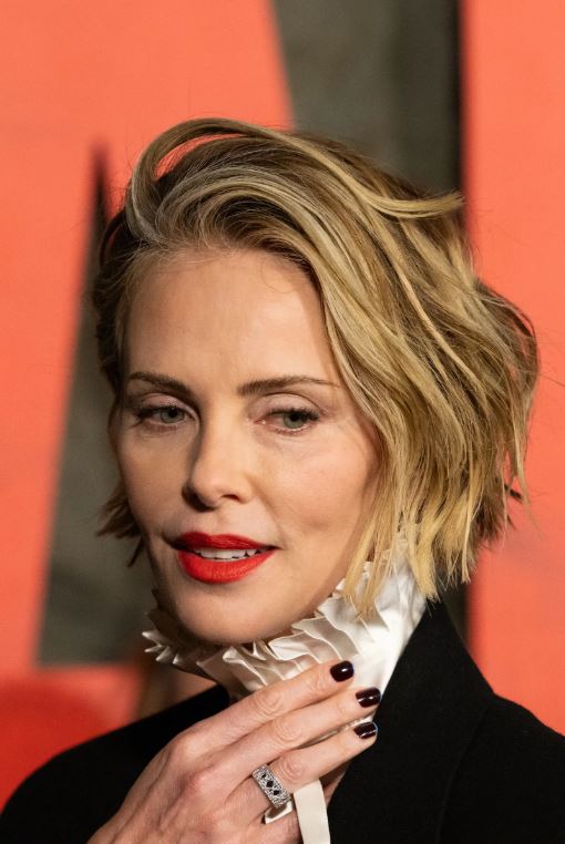 Charlize Theron wearing dark black cherry nails with a subtle blue micro-French tip at a red carpet event