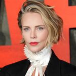 Charlize Theron wearing dark black cherry nails with a subtle blue micro-French tip at a red carpet event