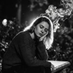 Emotional woman sitting alone at night looking at her phone while celebrity figures appear beside her, symbolizing public breakup drama and social media callouts.