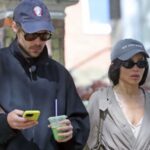Harry Styles and Zoë Kravitz walking in London wearing coordinated couple outfits with navy caps, trench coat, and casual street style