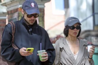 Harry Styles and Zoë Kravitz walking in London wearing coordinated couple outfits with navy caps, trench coat, and casual street style