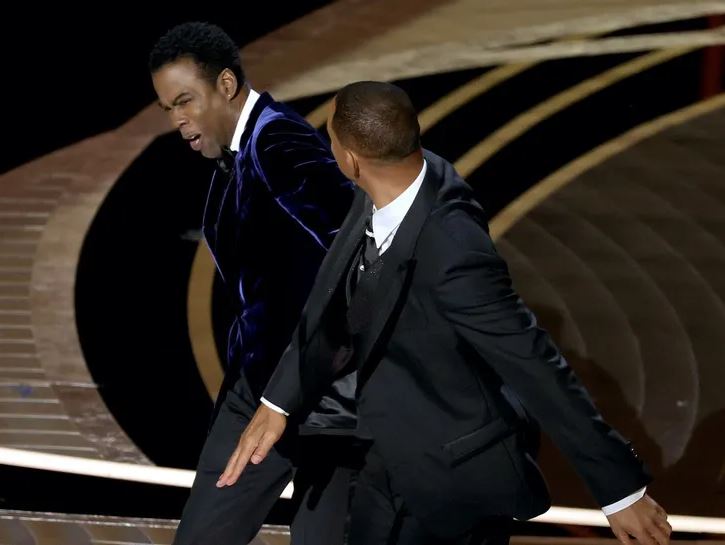 Close-up of Will Smith slapping Chris Rock on stage during the Academy Awards, with Jada Pinkett Smith visible in the audience reacting.