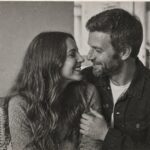 A black-and-white vintage-style photo of a smiling couple sitting closely on a couch, looking at each other affectionately, with visible film grain and worn edges resembling a 1976 photograph.