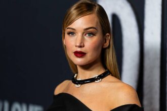Jennifer Lawrence wearing a black dress and brown coat, carrying a silver see-through statement shoulder bag on a night out