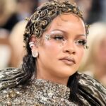 Rihanna at the 2026 Met Gala wearing a metallic Maison Margiela gown with gold makeup, glowing skin, glossy lips, and face gems