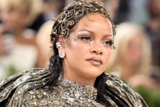 Rihanna at the 2026 Met Gala wearing a metallic Maison Margiela gown with gold makeup, glowing skin, glossy lips, and face gems