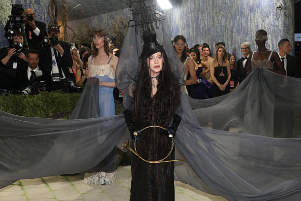 Madonna at the 2026 Met Gala wearing a brunette couture wig with textured waves, top hat, and veil inspired by Ray of Light era