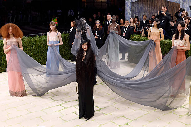 Madonna at the 2026 Met Gala wearing a brunette couture wig with textured waves, top hat, and veil inspired by Ray of Light era