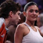 Kylie Jenner and Timothée Chalamet kissing courtside at a New York Knicks game at Madison Square Garden while wearing matching orange jackets and jeans
