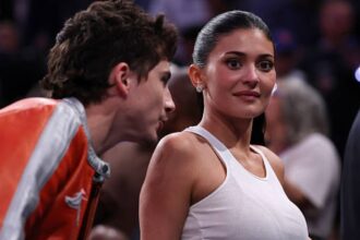 Kylie Jenner and Timothée Chalamet kissing courtside at a New York Knicks game at Madison Square Garden while wearing matching orange jackets and jeans
